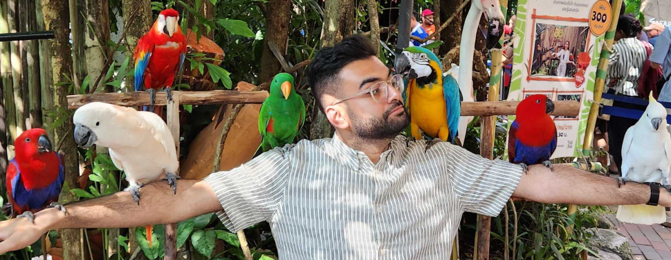 Zohaib sitting with with arms extended with colourful parrots sitting on his arms